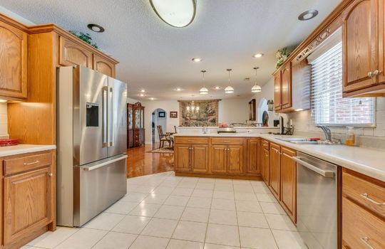 kitchen view toward dining space, tile flooring, dishwasher, sink, refrigerator, recessed lighting, bar seating, cabinets, countertops