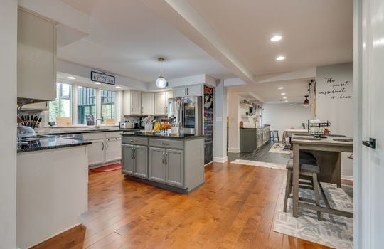 dining space, kitchen, recessed lighting, hardwood flooring, view into game room, cabinets, granite countertops, refrigerator, large windows above sink, sink