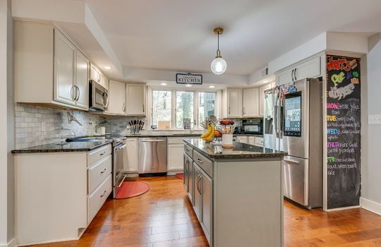 kitchen, tile backsplash, cabinets, granite countertops, sink, oven/range, built in microwave, refrigerator, hardwood flooring, large windows above sink