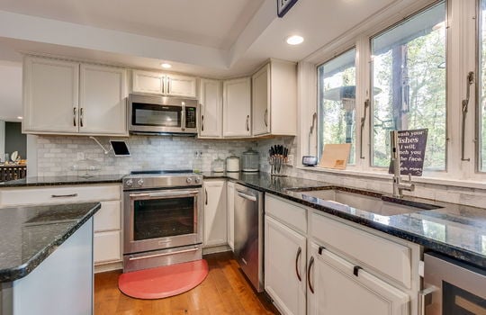 kitchen, kitchen island, oven/range, built in microwave, sink, dishwasher, wine refrigerator, large windows above sink, cabinets, granite countertops, hardwood flooring