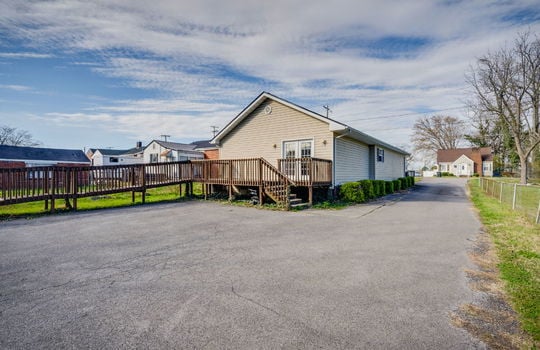 ramp, handicap accessible access, wood railings, wood deck, back door, vinyl siding, parking lot, wood stairs, driveway, landscaping