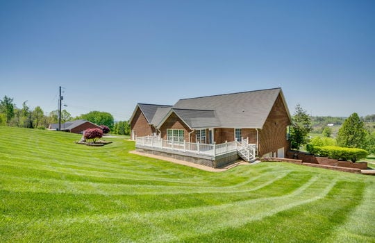 back view of property, two story brick home, back deck, two car drive under garage, roof, landscaping