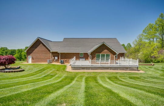 back view of home, back deck, brick exterior, exterior entry doors, landscaping plants and rock, trees