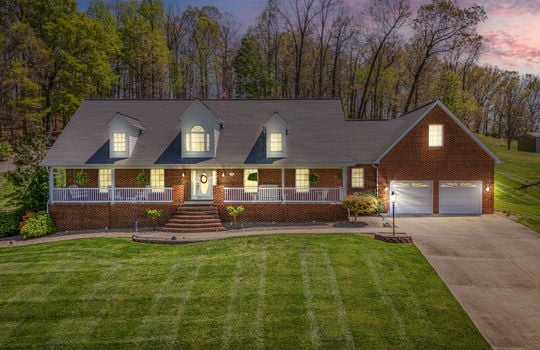 twilight photo, brick, two story home, covered front porch, brick porch steps, landscaping, two car garage, driveway, trees