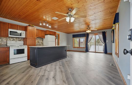 Kitchen, cabinets, countertops, kitchen island, luxury vinyl flooring, door to balcony, wood ceiling, ceiling fans, microwave, oven/range, sink, refrigerator, windows