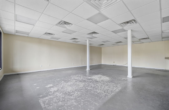 Open space, concrete flooring, ceiling tiles, fluorescent lighting, pillars, window