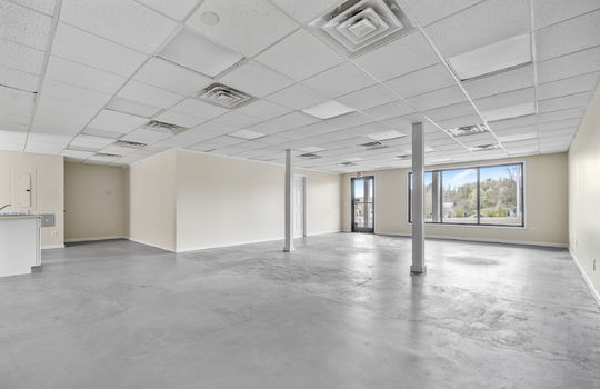 open area for retail space, commercial space for lease, large window, door, pillars, concrete flooring, ceiling tiles, fluorescent lighting