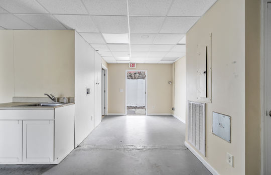 utility/storage area, concrete flooring, sink, cabinet, ceiling tile, fluorescent lighting, exterior door, back door
