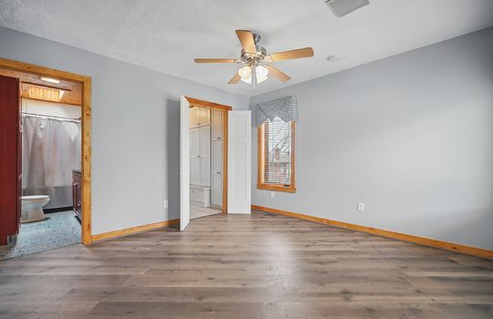 bedroom, door to bathroom, door to walk in closet, ceiling fan, luxury vinyl flooring, windows