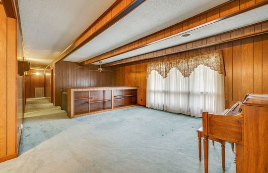 living room, carpet, built in shelving, large windows, ceiling beams, hallway, paneling walls