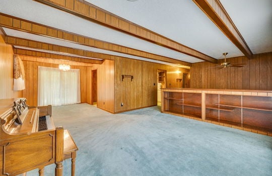 living room, carpet, ceiling beams, ceiling fan, dining space, large gladd door, entry to kitchen, hallway, paneling walls, built in shelving