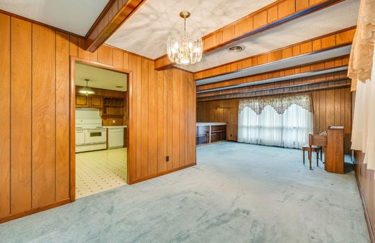 dining space view toward kitchen and living room, carpet, ceiling beams, chandelier, built in shelving, windows, vinyl flooring in kitchen