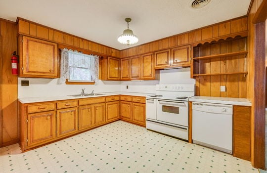 kitchen, paneling walls, vinyl flooring, wood cabinets, window above sink, sink, countertops, shelving, dishwasher, oven/range