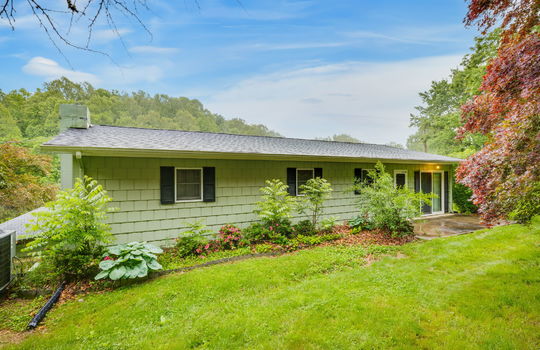 back of home, wood paneling, windows, exterior door, sliding glass door, rear patio, landscaping, trees