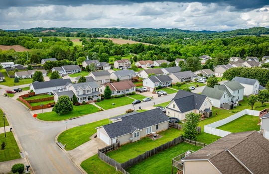 aerial view from back of home, fenced back yard, roof, driveway, garage, front yard, neighboring homes, road, mountains