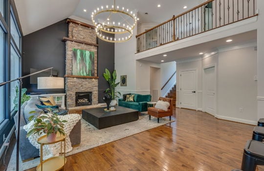 living room, stairs, stairs to upper level, catwalk, stone fireplace, vaulted ceilings, chandeiler, picture windows, hardwood flooring