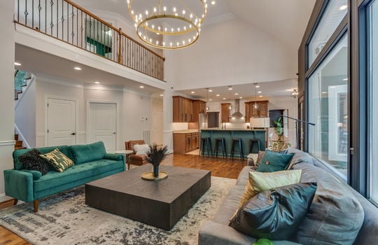 living room, stairs to upper level, hardwood flooring, chandelier, view into kitchen, windows, view of upper level catwalk