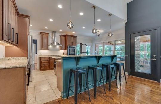 kitchen, tile flooring, cabinets, granite countertops, double wall oven, refrigerator, cooktop, sink, kitchen island, sink in island, kitchen sink, granite countertops, recessed lighting, bar seating, door to sunroom