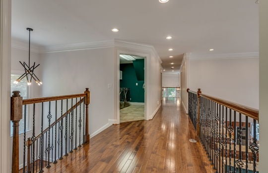 upper level walkway, railings, catwalk, hardwood flooring, door to laundry room, recessed lighting, vaulted ceilings