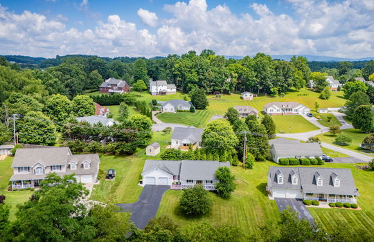 aerial photo of property from front yard, trees, ranch style home, driveway, two car attached garage, covered front porch, neighboring homes, mountains