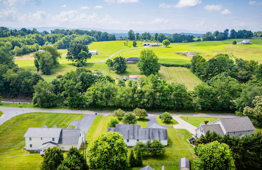 aerial photo of property from back yard, trees, ranch style home, driveway, two car attached garage, back deck, neighboring homes, road