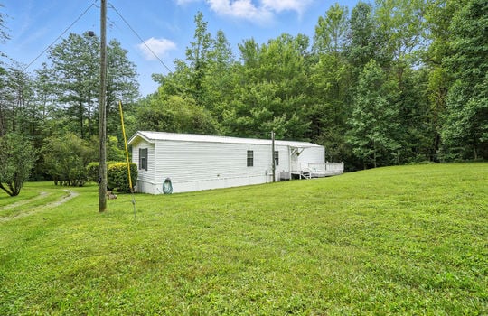 back yard, back view of singlewide, metal roof, back door, back deck, trees, landscaping