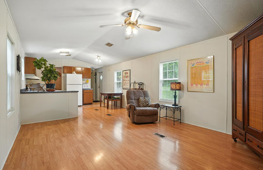front door view of living room and kitchen, windows, laminate flooring, ceiling fan, kitchen, cabinets, countertops, refrigerator, back door, hallway