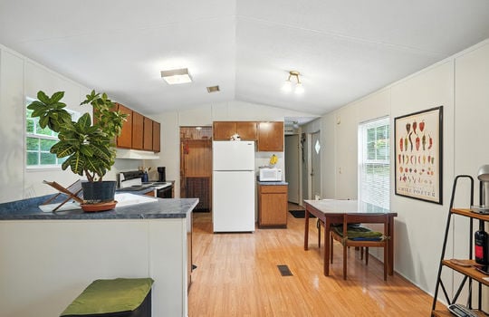 living room view toward kitchen, pantry, laminate flooring, cabinets, countertops, sink, oven/range, refrigerator, hallway to primary bedroom