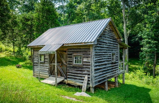 rustic cabin, covered porch, cleared land, trees