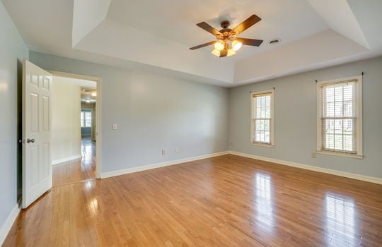 primary bedroom, tray ceiling, hardwood flooring, ceiling fan, door to hallway, windows