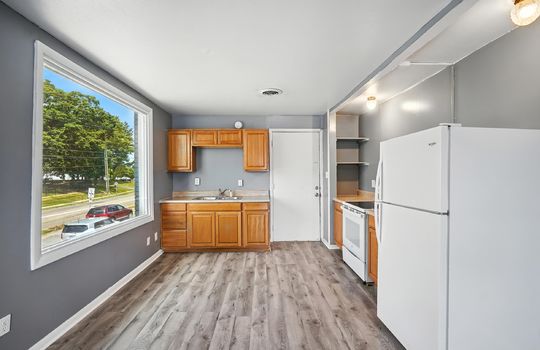 studio apartment, kitchen space, cabinets, sink, countertops, range, refrigerator, luxury vinyl flooring, large picture window