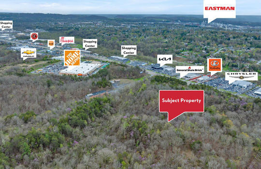 aerial photo, property marker for subject property, property markets for neighboring businesses: home depot, chevrolet, chick-fil-a, Chipotle, Kia, General Shale, Kubota, Chrysler, Mercedes-Benz, Eastman, Stone Drive, mountain views, trees, undeveloped land