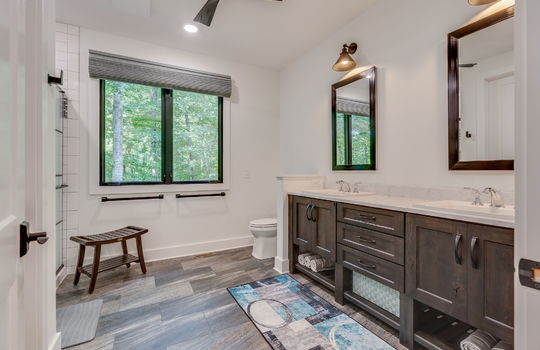 primary bathroom, double vanity sinks, cabinets, toilet, tiled shower, tile floor, window