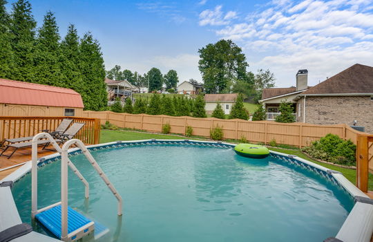 Pool with deck surround, fully fenced back yard, back of home, vinyl siding, brick, storage shed, landscaping