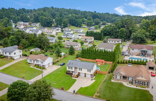 Aerial photo of home and surrounding properties, mountain views, split foyer, brick, vinyl siding, two car garage, driveway, steps to front door, front yard, fenced back yard, pool, storage shed