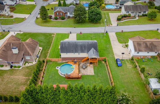aerial view over back yard toward front yard, fenced back yard, pool deck, covered back deck, landscaping, back yard, front yard, driveway, road, surrounding properties