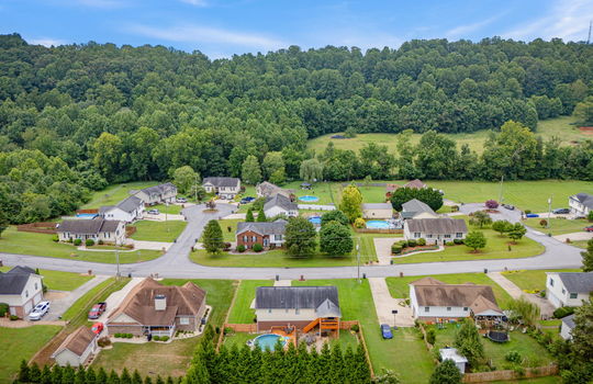 aerial view over back yard toward front yard, fenced back yard, pool deck, covered back deck, landscaping, back yard, front yard, driveway, road, surrounding properties, mountain views