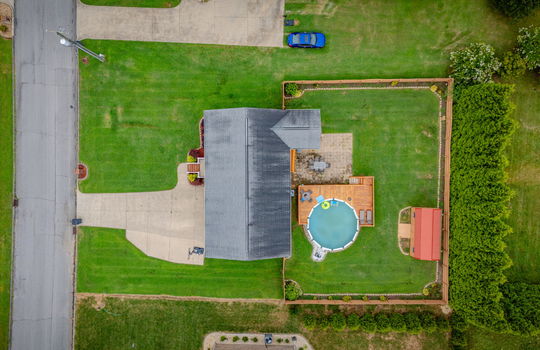 overhead aerial view of property, driveway, roof, front steps, back yard, covered back deck, patio pavers, pool with deck, storage shed, landscaping