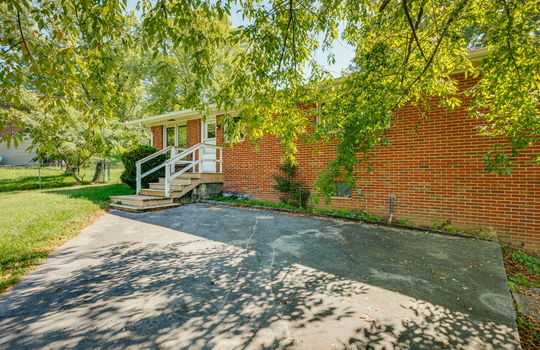back of home, brick ranch for lease, back yard, trees, landscaping, front steps, storm door, front door, windows, concrete parking pad