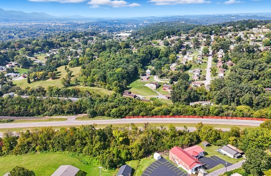 aerial view of property toward road, wooded property, nearby interstate, nearby road, nearby homes, mountain views, nearby parking/businesses