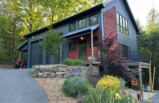 guest home. garage doors, driveway, metal siding, front door, landscaping