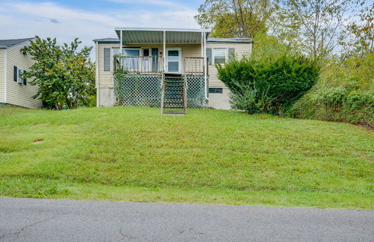 street view of home, stairs to covered front porch, fixer upper, front door, vinyl siding, trees, neighboring home