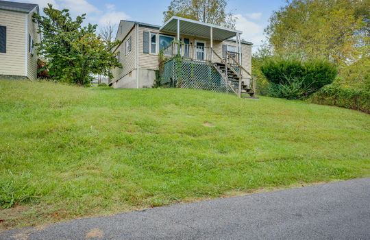 street view of home, stairs to covered front porch, fixer upper, front door, vinyl siding, trees, neighboring home