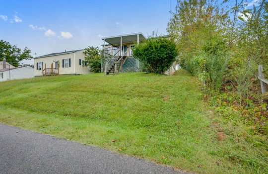 street view of home, stairs to covered front porch, fixer upper, front door, vinyl siding, trees, neighboring home