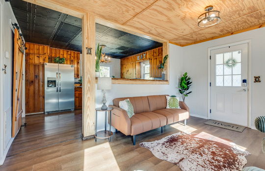 living room, kitchen, front door, beadboard ceiling, kitchen ceiling tiles, cabinets, refrigerator, luxury vinyl flooring