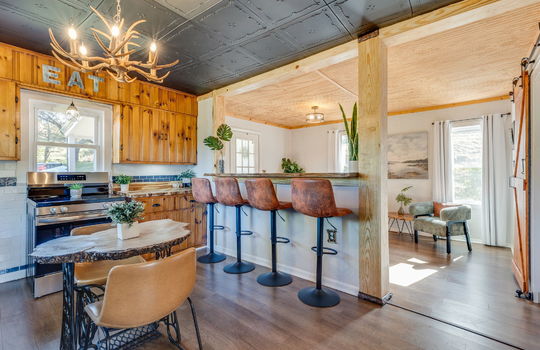 kitchen, bar seating overlooking living room, luxury vinyl flooring, stainless steel stove,wood cabinets, butcher block, tile backsplash, windows, decorative ceiling tiles