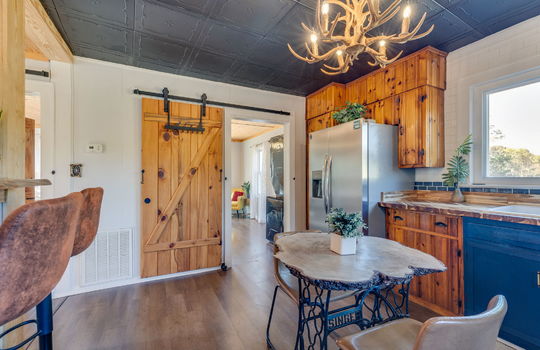 kitchen, decorative ceiling tiles, luxury vinyl flooring, butcher block/wood countertops, wood cabinetry, stainless steel refrigerator, sink, window, barn door, bar seating