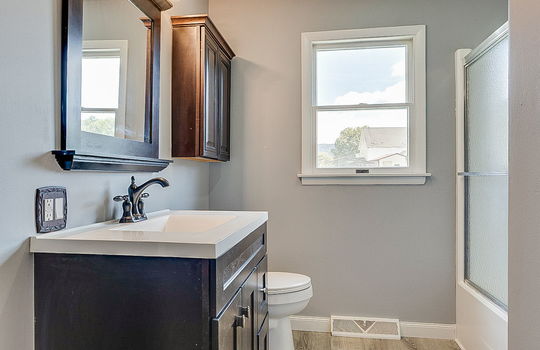 bathroom, shower/tub, glass shower door, sink, toilet, laminate flooring, window, cabinet