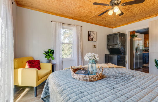 bedroom, beadboard ceiling tile, luxury vinyl flooring, windows, ceiling fan, stacked washer/dryer hookup, door to kitchen