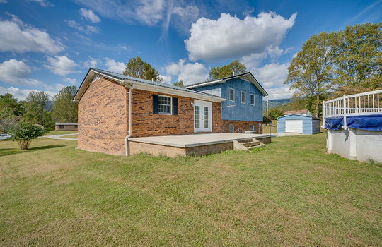 back side view of home, brick exterior, wood siding, back patio, back yard, gated/fenced above ground pool, garage, carport, gravel driveway, side yard